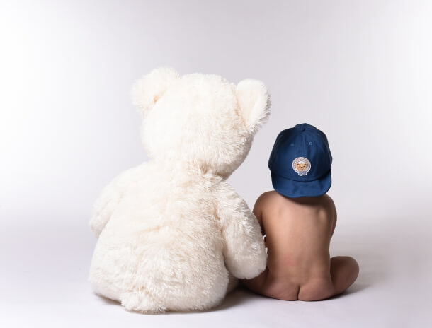 Bebis med keps bredvid sin nalle, kreativ barnfotografering.