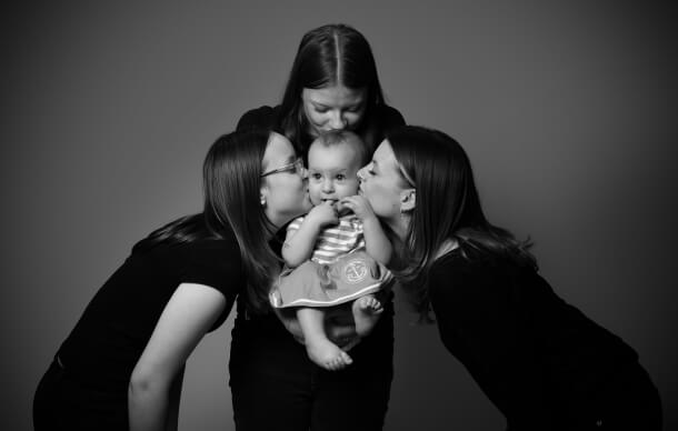 Konstnärlig svartvit bild på syskon som håller sin yngsta tätt, familjefotografering.