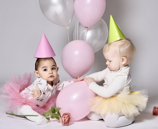 Två små barn i partyhattar med ballonger och konfetti, festlig barnfotografering.