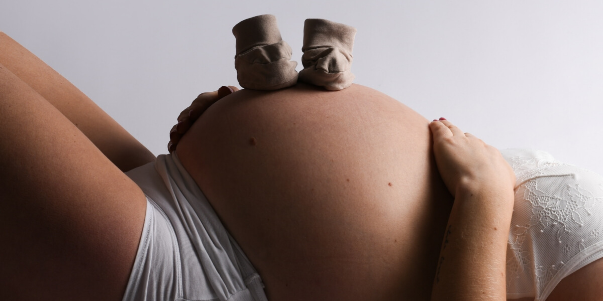 Närbild av en gravid kvinna som ligger ner med ett par små babyskor placerade på sin mage